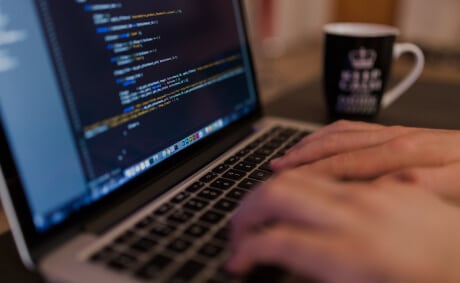 KICS_Professionelle-Softwareentwicklung-und-Coding Entwicklerhände am Laptop mit geöffnetem Code-Editor und sichtbarem Programmiercode.